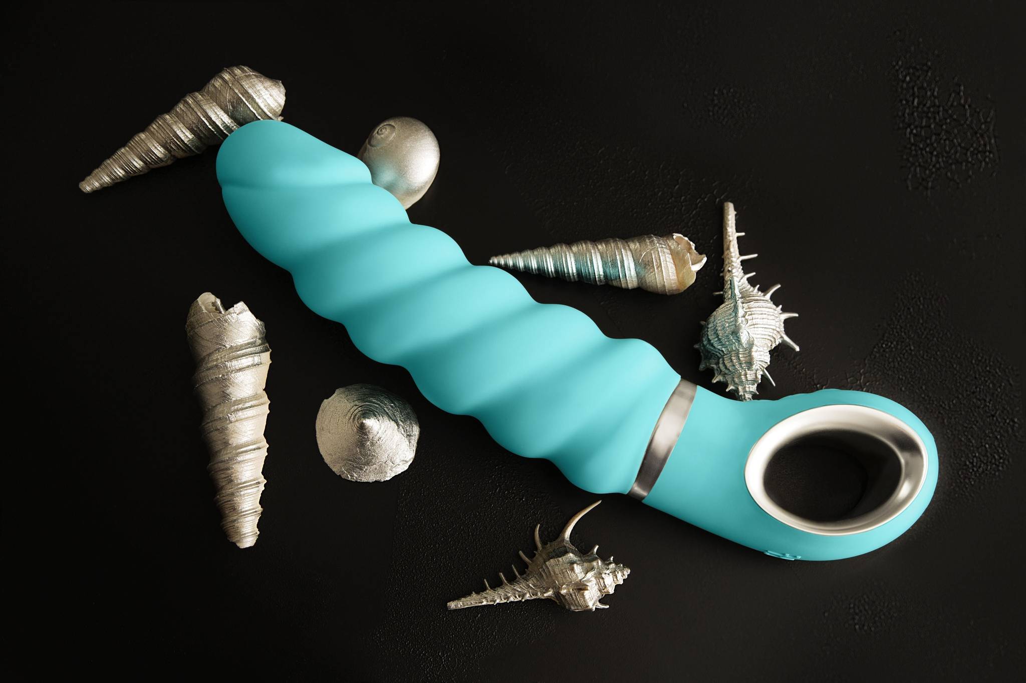 Turquoise silicone adult toy with silver metallic band and handle surrounded by seashells for quality comfort confidence
