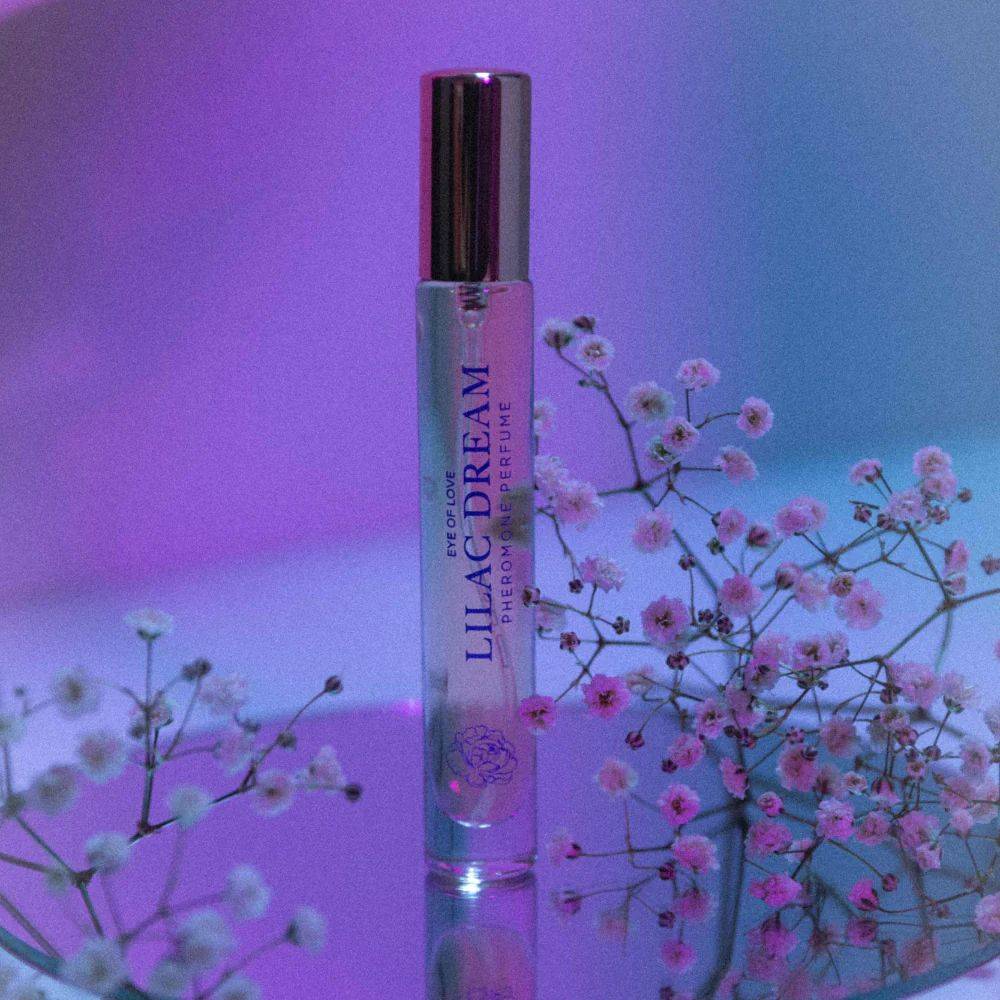 A slender transparent glass rollerball perfume bottle with a gold cap labeled lilac dream by eye of love for daily body care