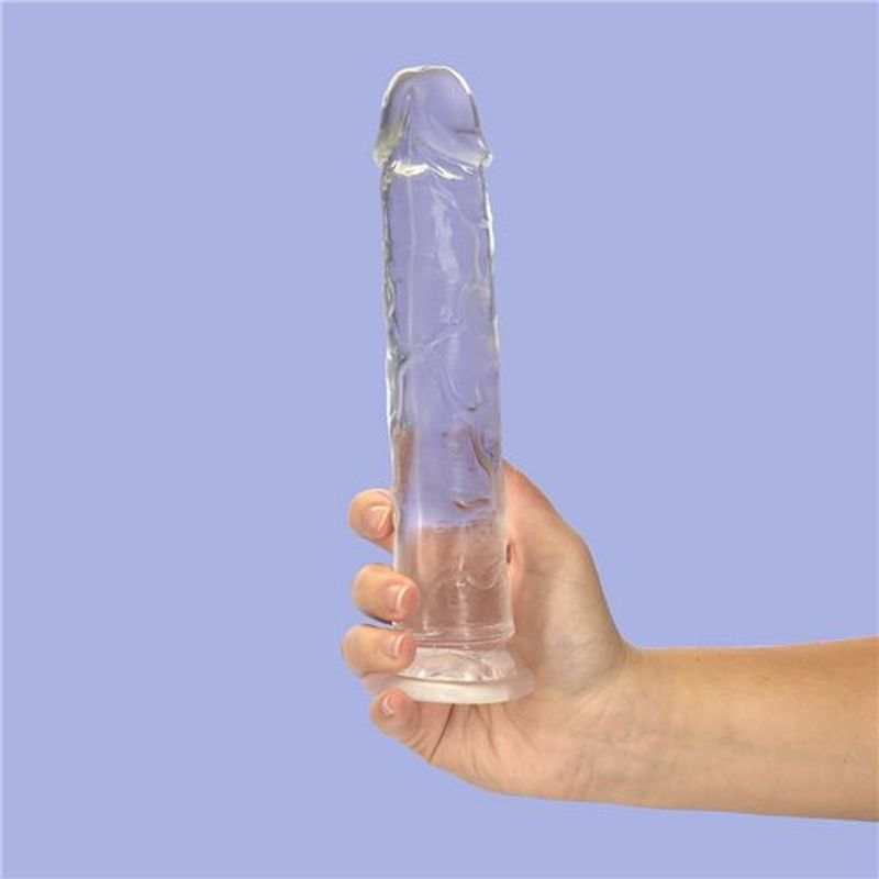 Addiction Crystal clear silicone dildo held against lavender background, showing smooth texture and sculpted tip.