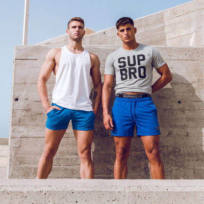 Two athletic men in SUPAWEAR activewear shorts and tank tops posing outdoors — SUPAWEAR men's collection