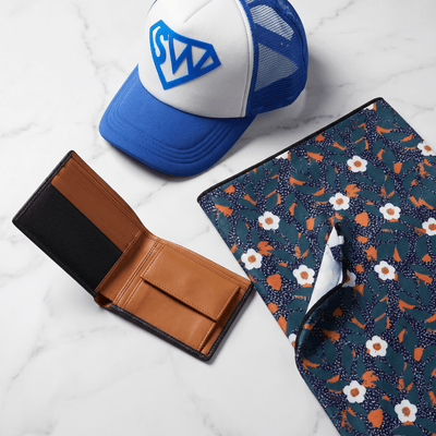 Accessories (Men's) collection — leather wallet, patterned beach towel, and trucker cap styled flatlay