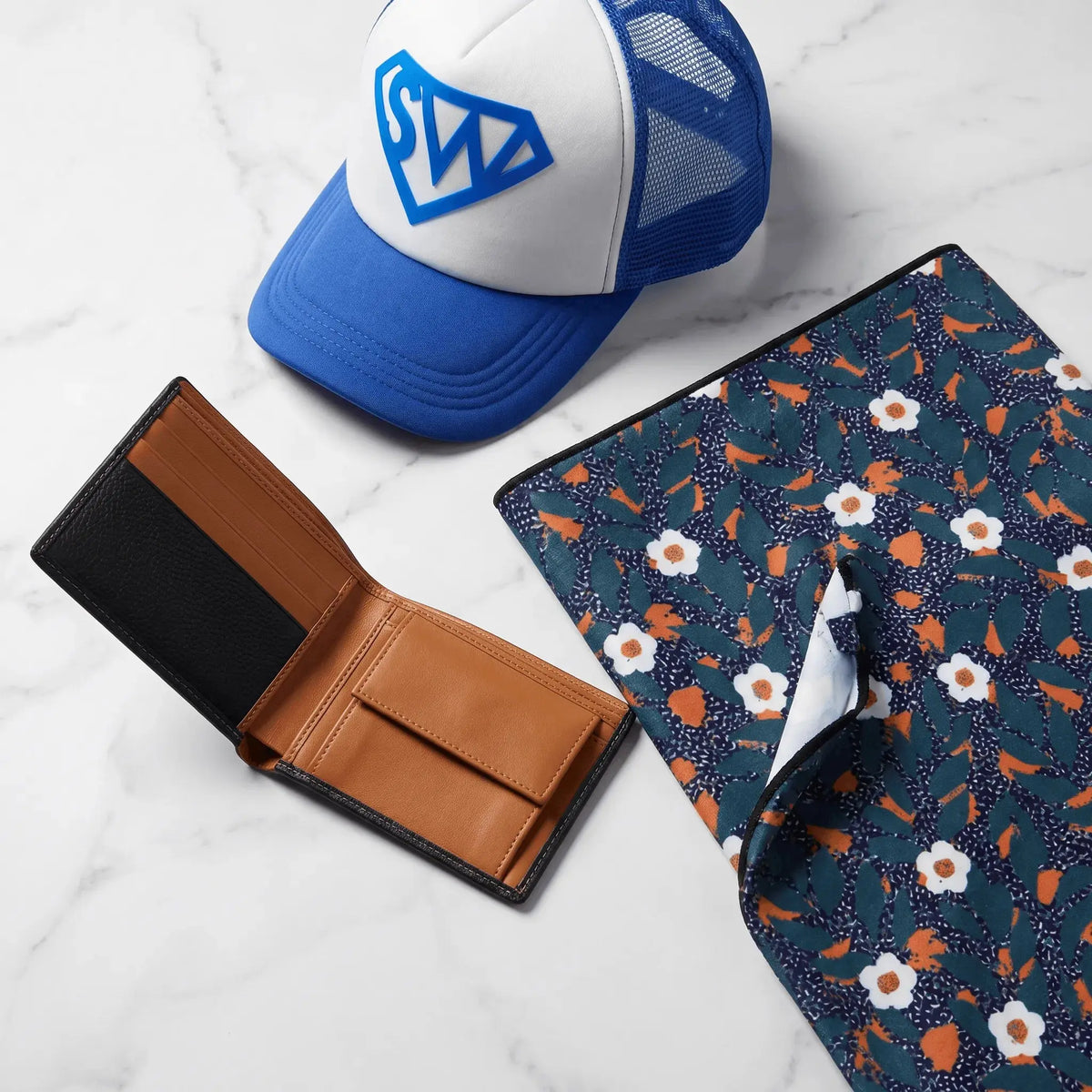 Accessories (Men's) collection — leather wallet, patterned beach towel, and trucker cap styled flatlay
