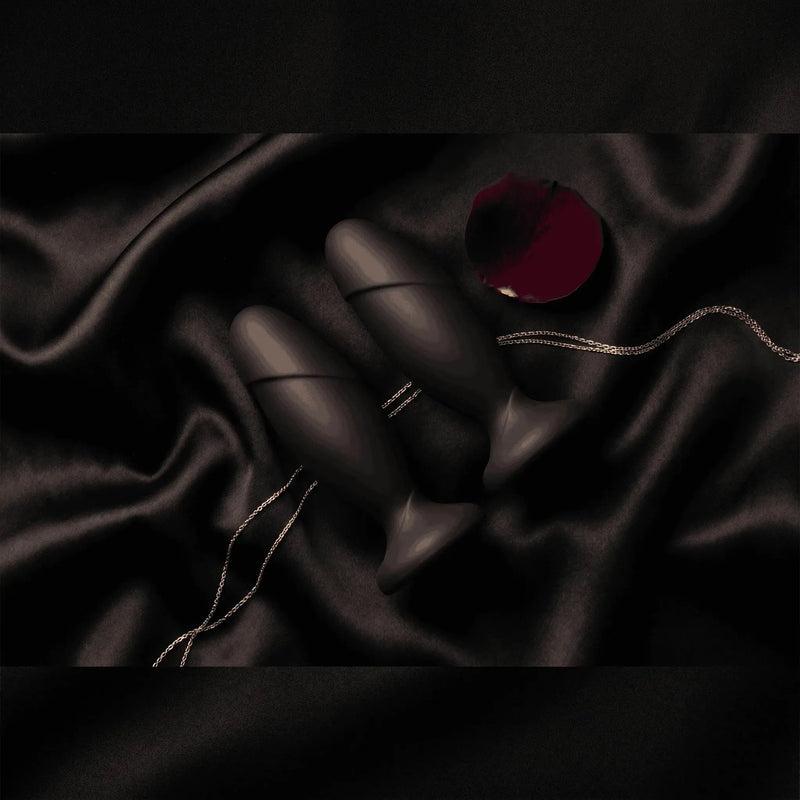 Anal Adventures black silicone anal plugs on black satin with rose petal, dark luxury editorial flat lay