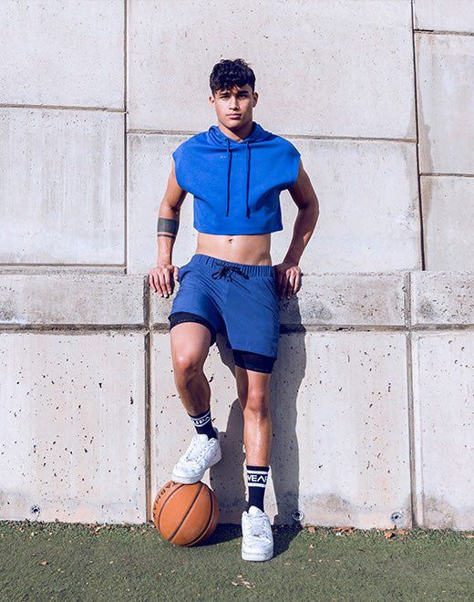 Male model in royal blue training shorts with compression layer, posed with a basketball — men's performance activewear.