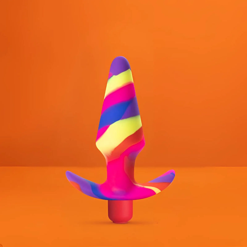 Avant Free Spirit swirling rainbow silicone butt plug with bullet vibrator on a vibrant orange background.