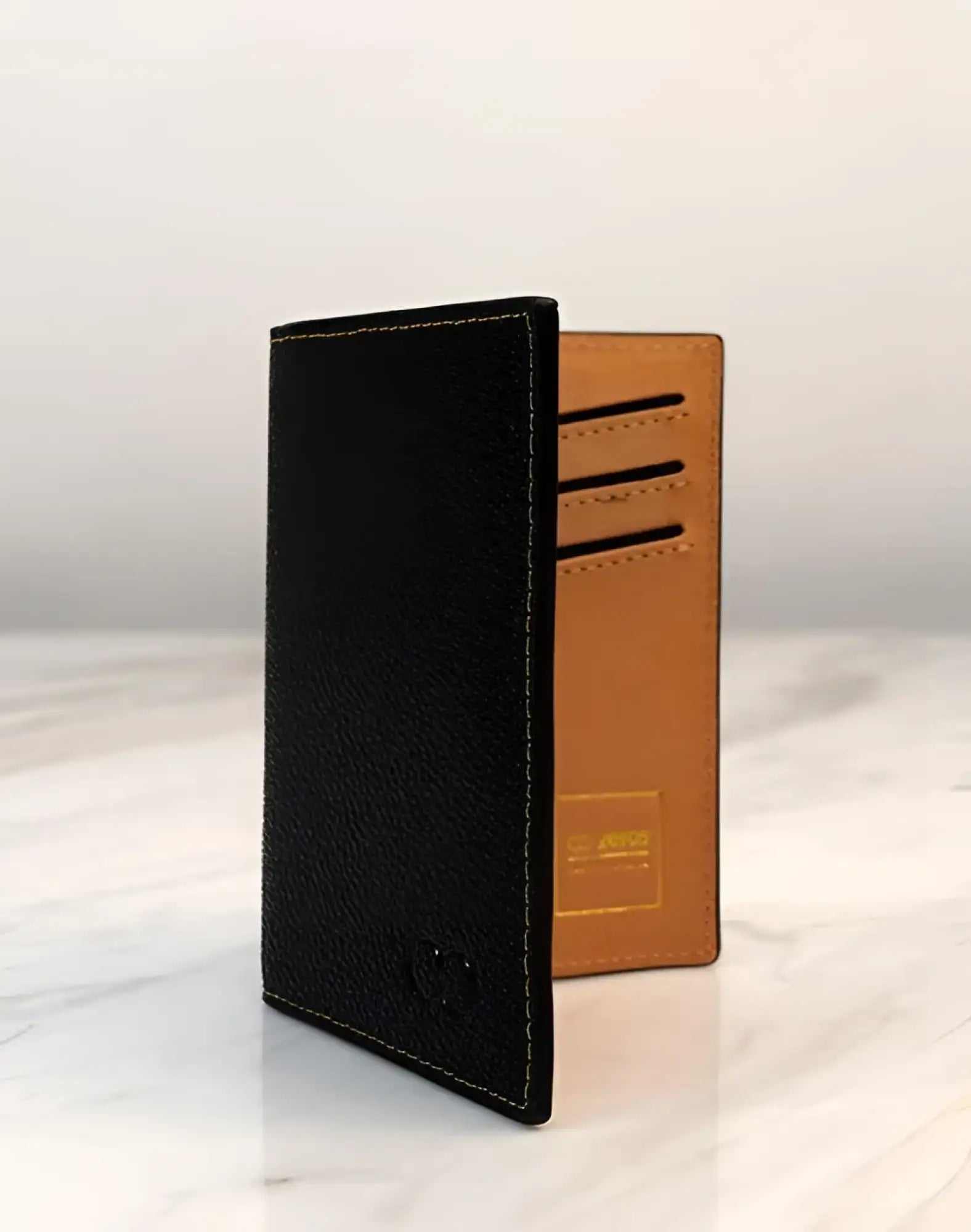 2EROS RFID Icon passport wallet open on marble — black pebble leather with caramel tan interior and card slots.