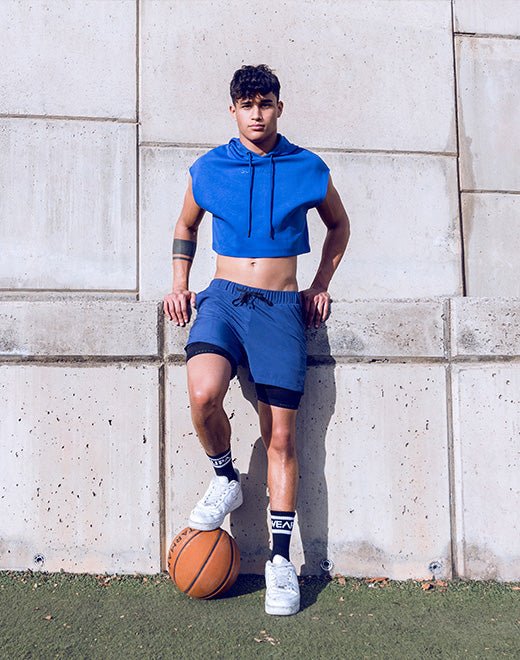 Male model in royal blue training shorts with compression layer, posed with a basketball — men's performance activewear.