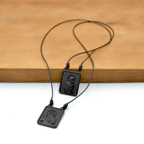 Two black cord necklaces with rectangular dark pendants on a wood surface.