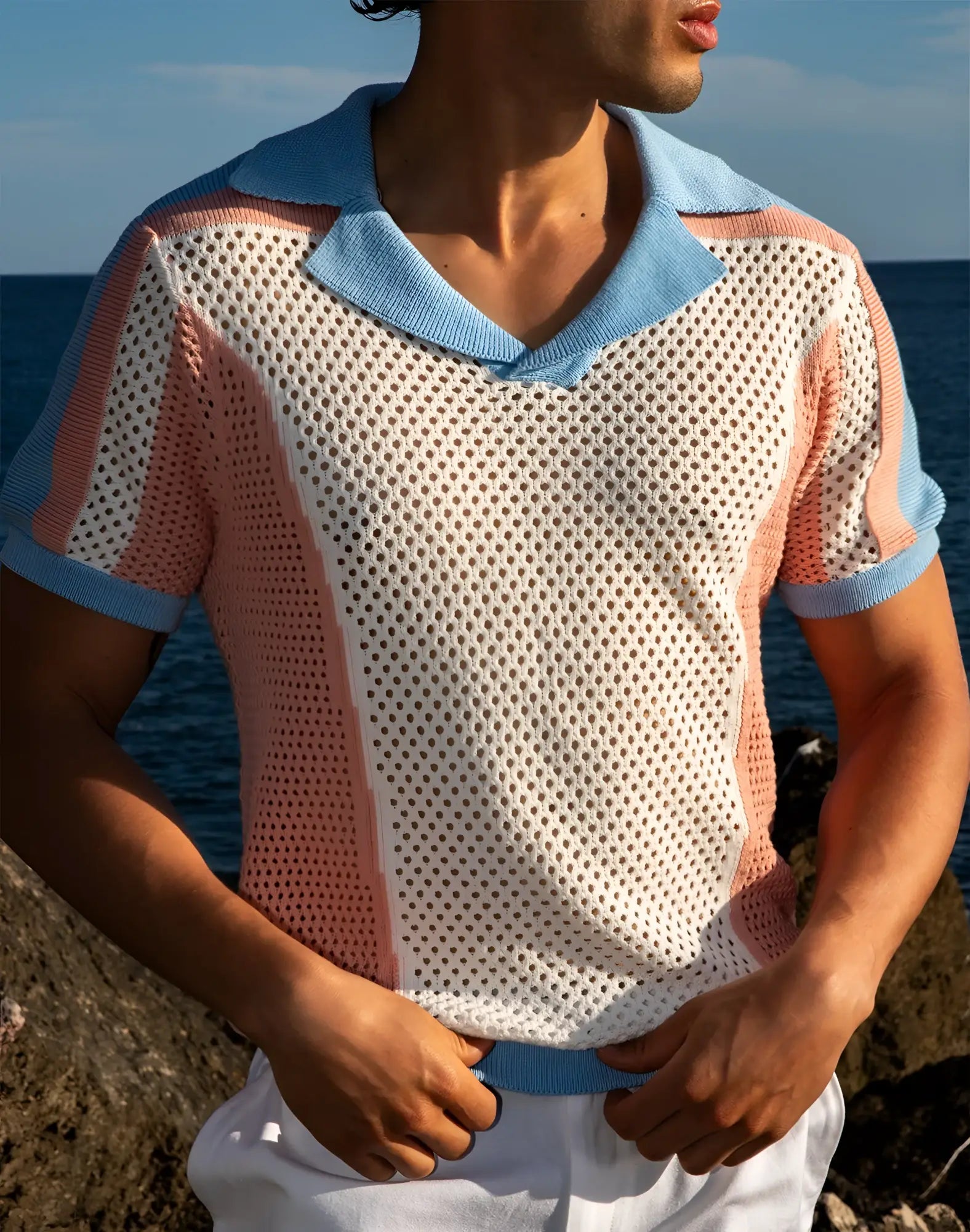 A man wearing a light blue and pink perforated knit 2EROS Aruba polo shirt with short sleeves