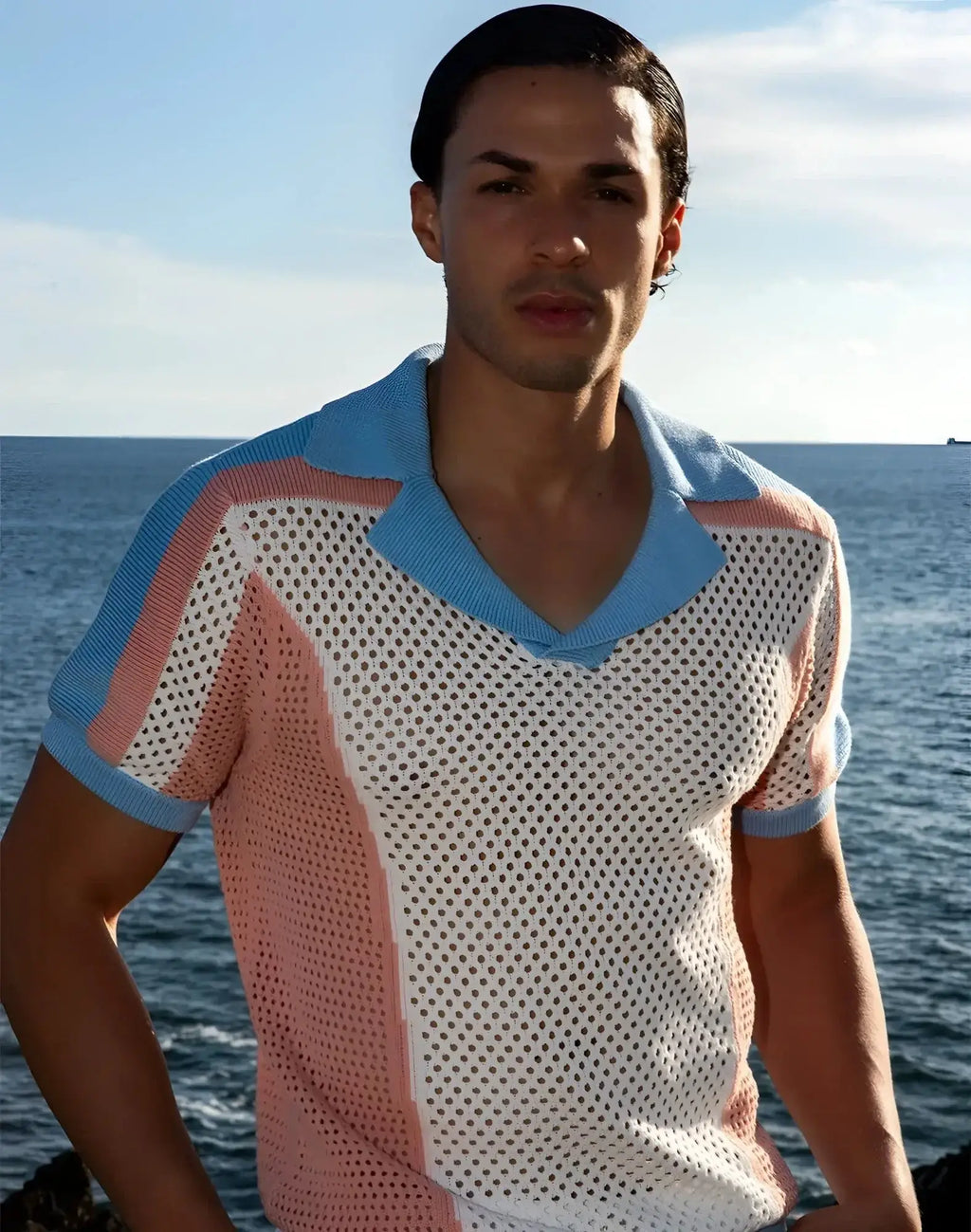 A man wearing a 2EROS Aruba polo short-sleeved v-neck knit shirt with white mesh body and pink blue accents