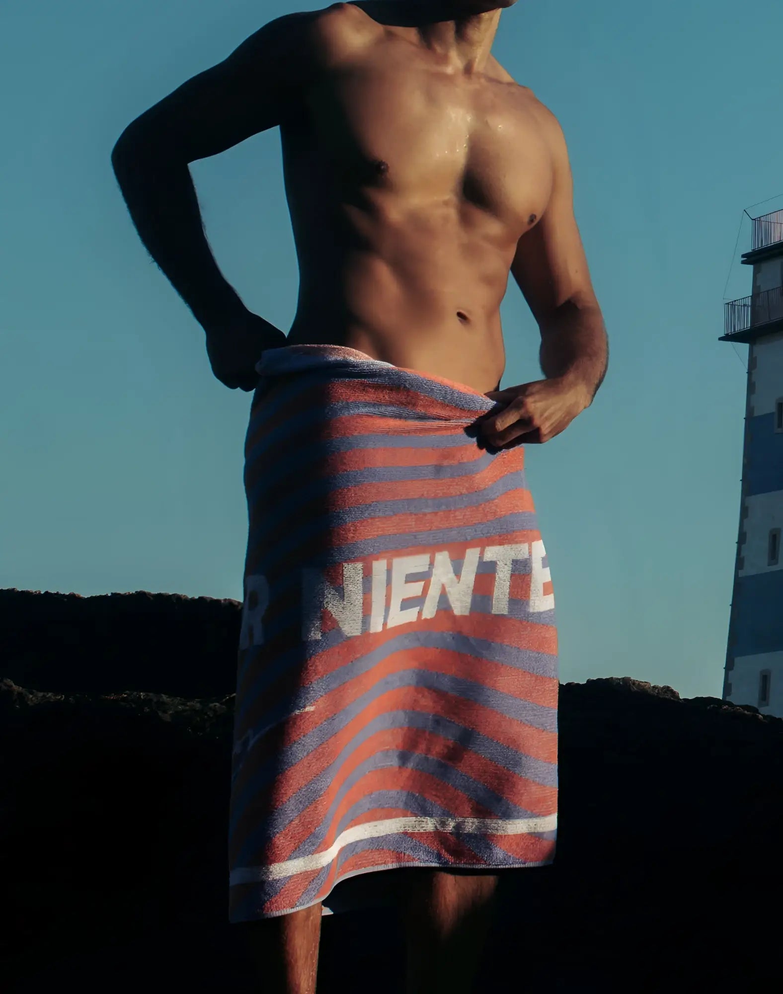 A vibrant orange and blue striped 2EROS beach towel with bold white lettering wrapped around a mans waist