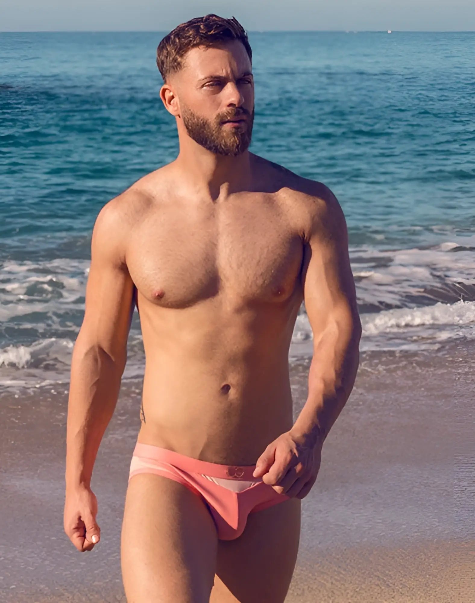 A man wearing coral 2EROS BLK Label No6 swim brief with subtle pattern designed for swimming and beachwear
