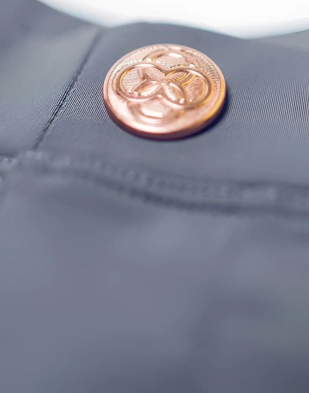 A copper-toned embossed button on dark gray fabric from 2eros bondi shorts series 3 alloy