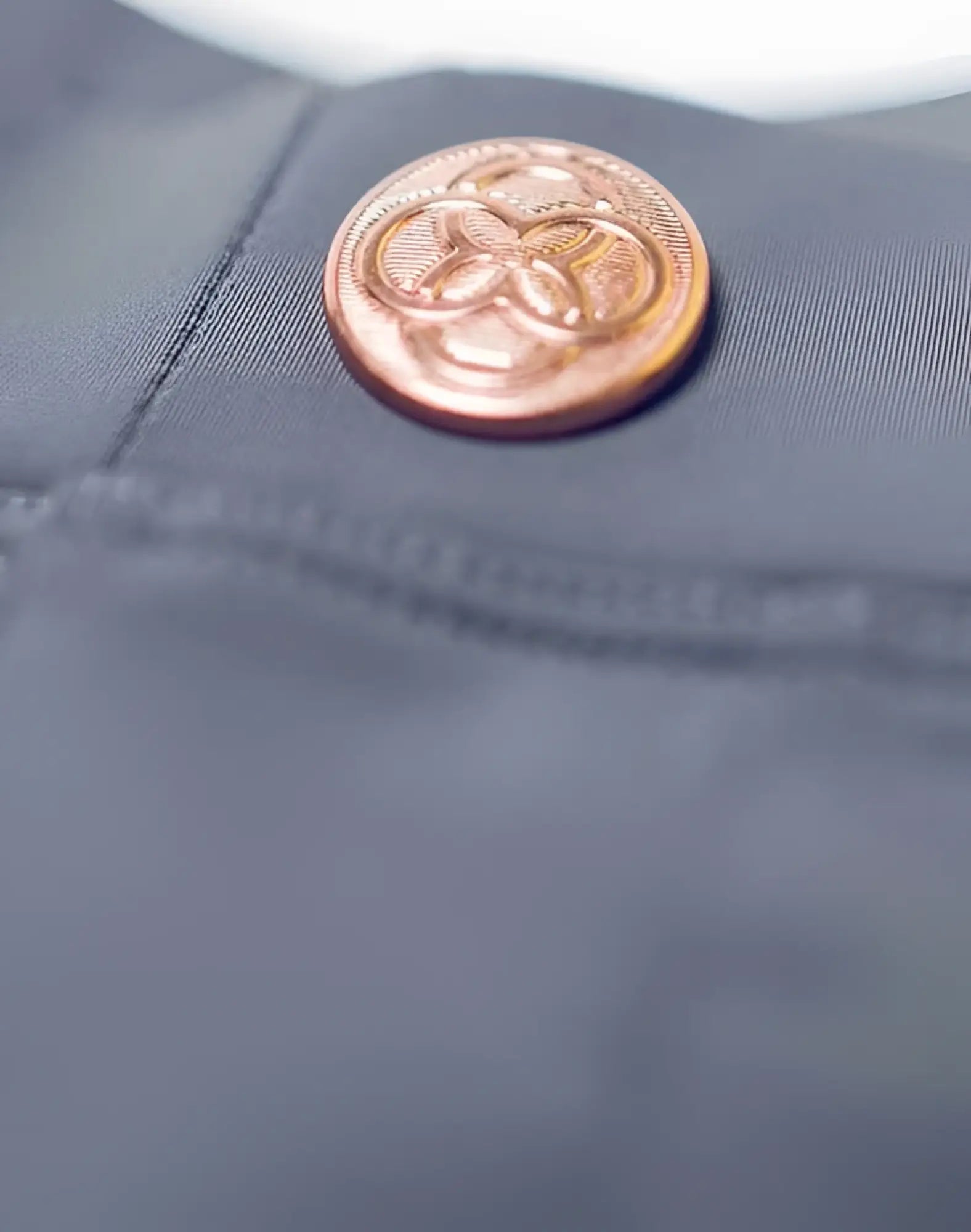 A copper-toned embossed button on dark gray fabric from 2eros bondi shorts series 3 alloy