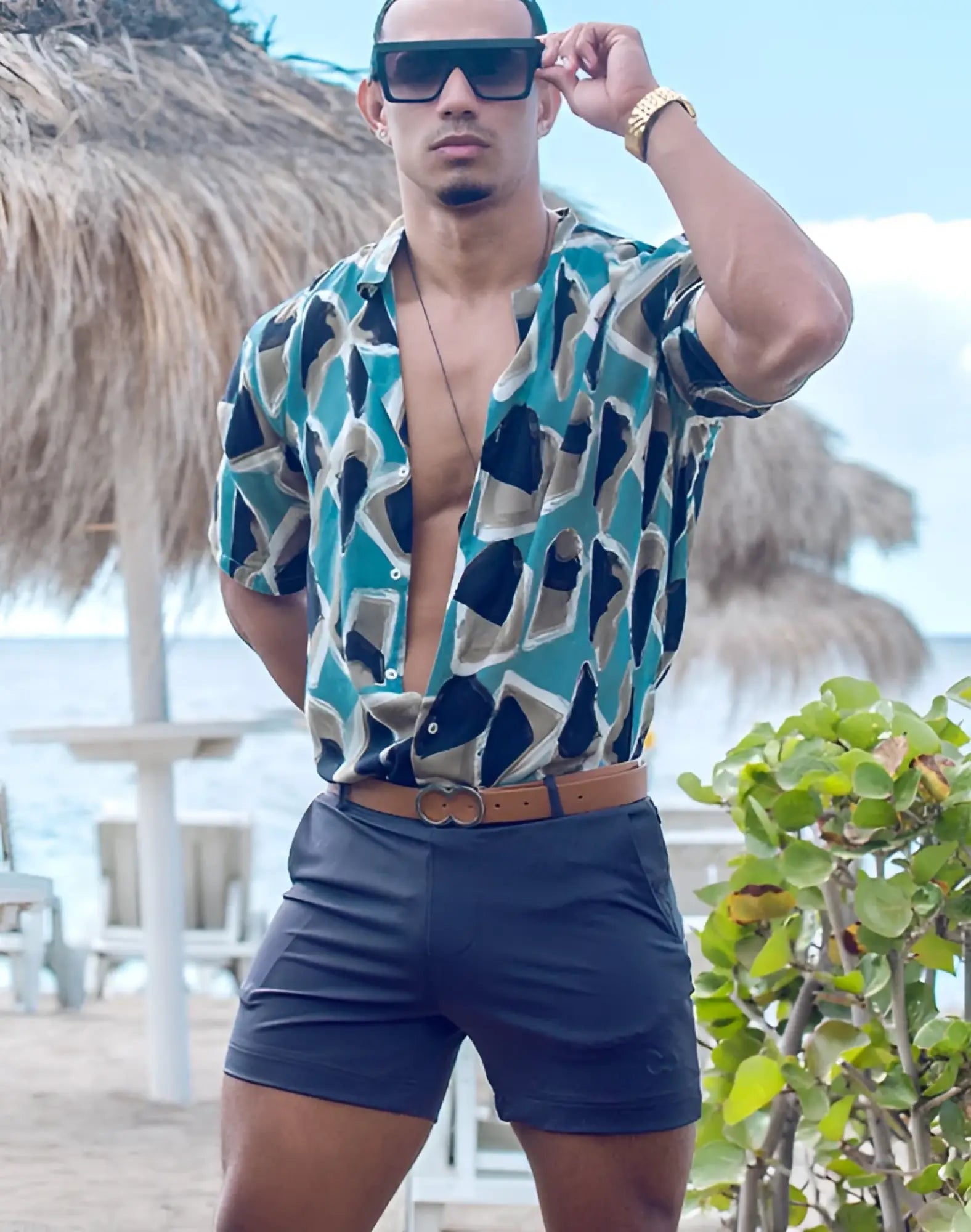 A man wearing a teal and black geometric patterned short sleeved shirt with 2EROS Bondi charcoal shorts