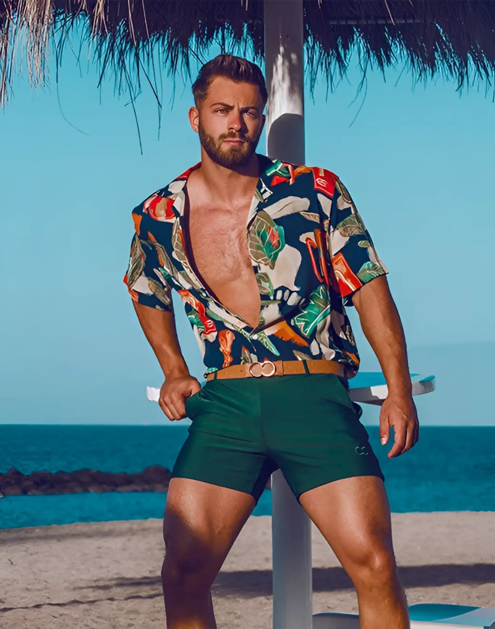 Man wearing 2eros bondi shorts series 3 in green with tan belt and tropical print short-sleeved shirt