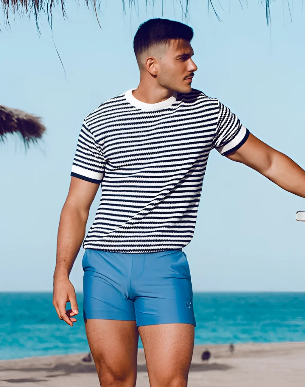 A man wearing 2EROS Bondi shorts pastel blue with black and white striped short-sleeved knit shirt and navy trim