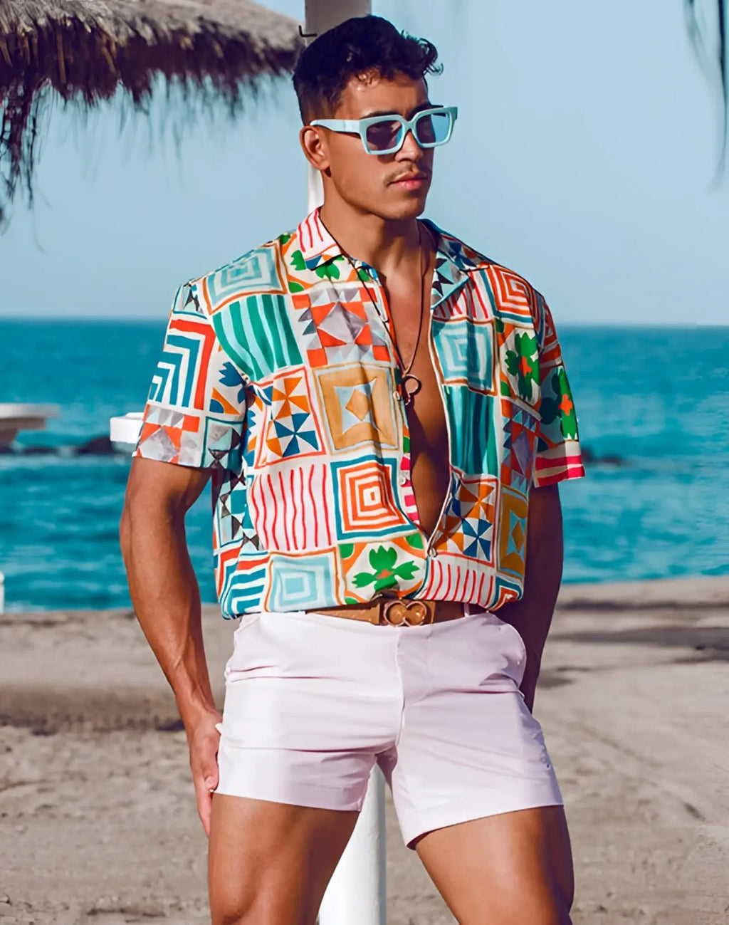 A man wearing a vibrant short-sleeved geometric pattern shirt paired with pastel pink 2EROS Bondi Shorts Series 3