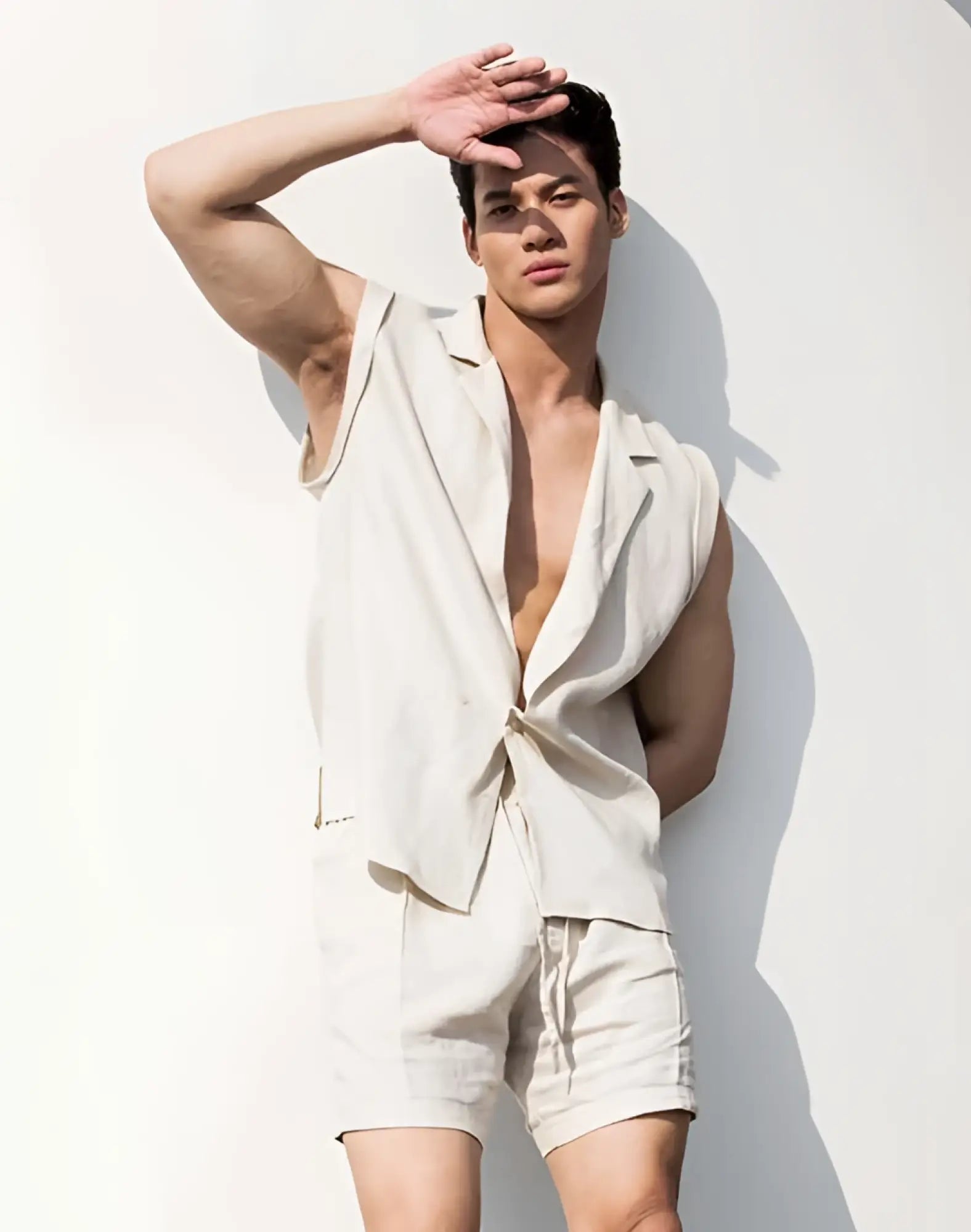 A man wearing a beige 2EROS breezy linen single button wrap vest with tied front and matching shorts