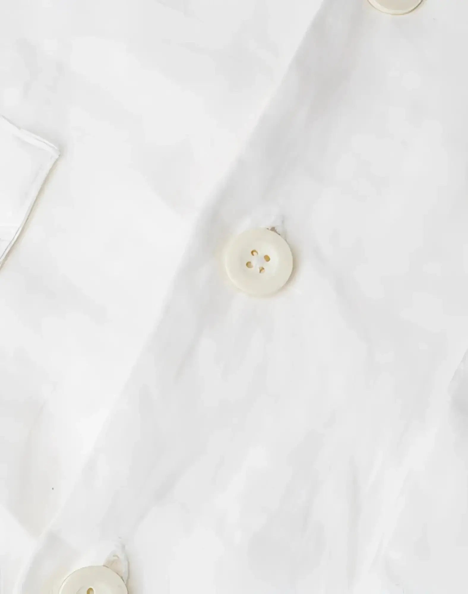 Cream-colored round button with four holes and subtle sheen on 2eros cropped white linen shirt