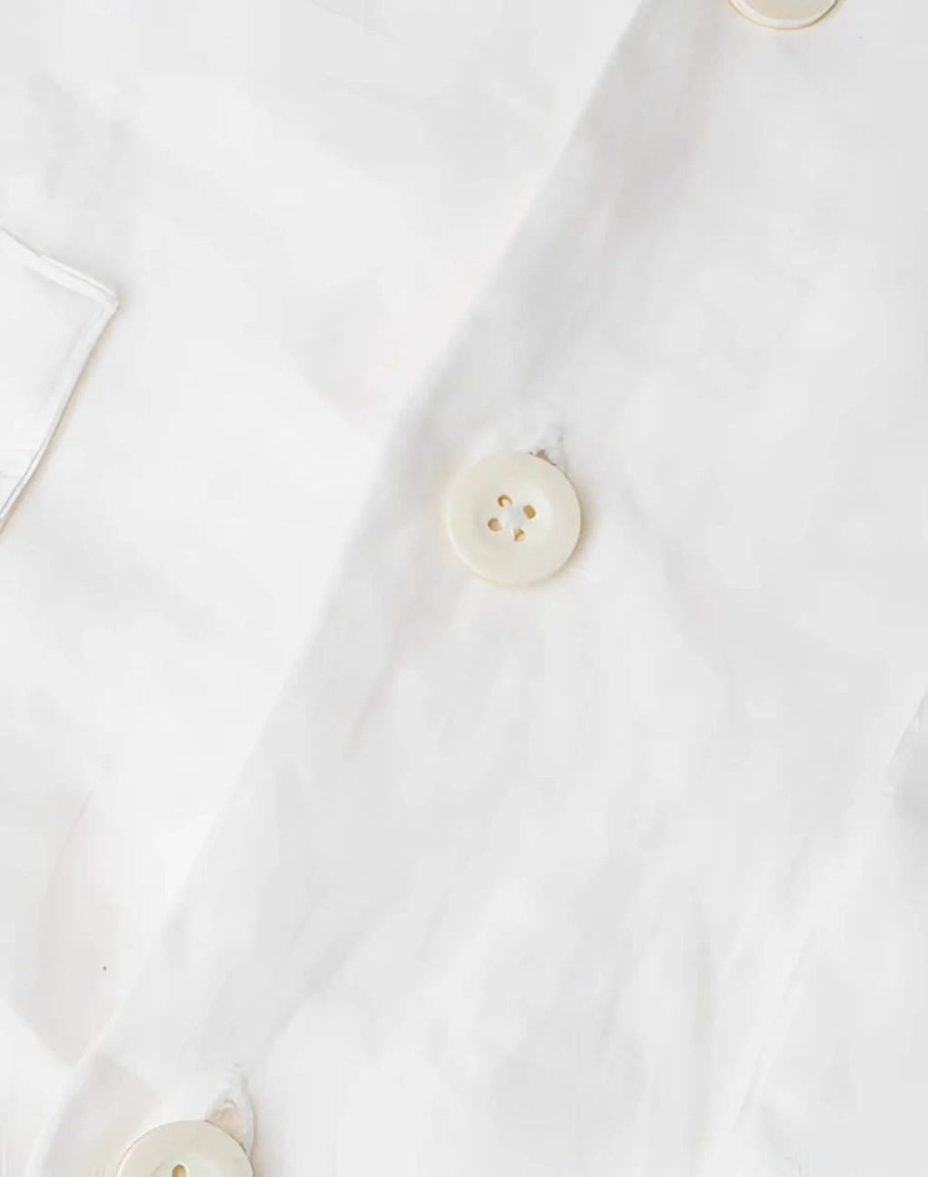 Cream-colored round button with four holes and subtle sheen on 2eros cropped white linen shirt
