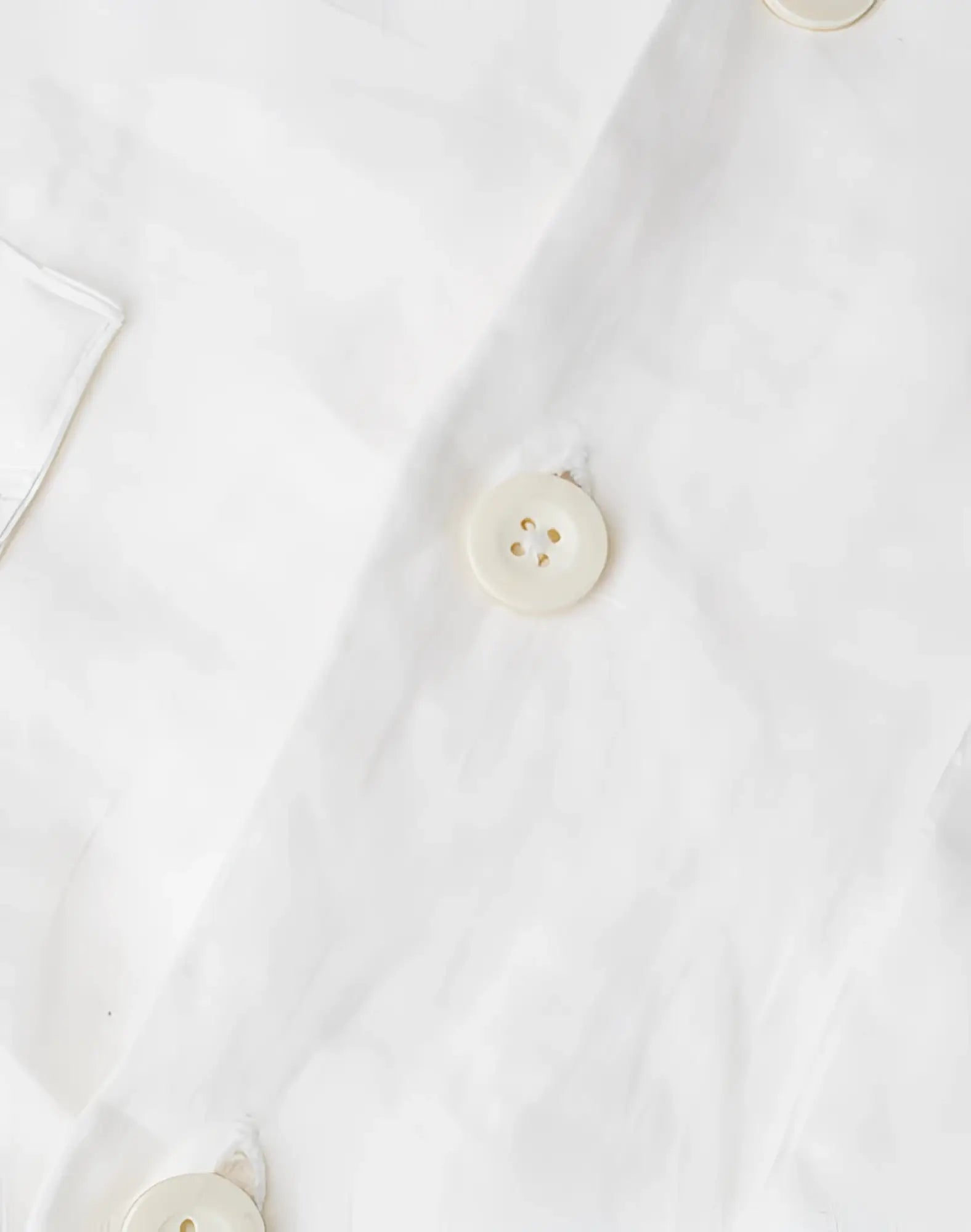 Cream-colored round button with four holes and subtle sheen on 2eros cropped white linen shirt