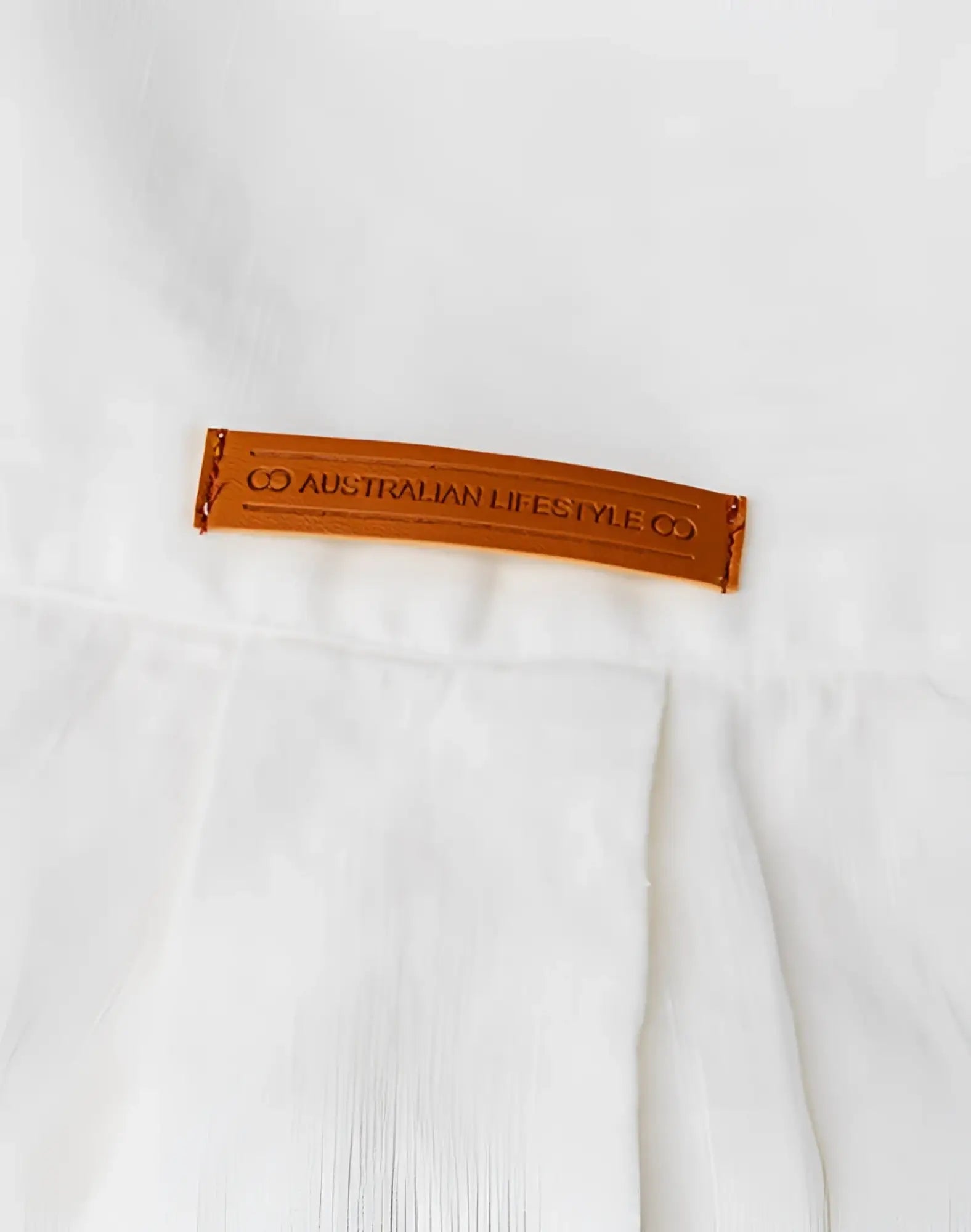 A tan leather brand tag embossed with co australian lifestyle co stitched on a white 2eros cropped linen shirt