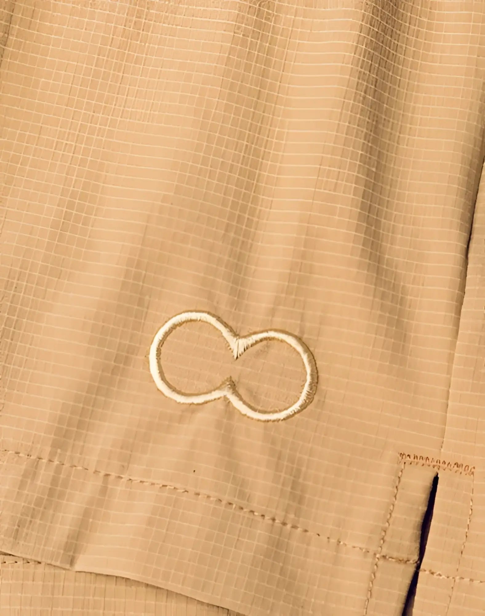 Beige infinity symbol embroidered on textured light tan fabric of 2EROS Hamilton shorts hazelnut back side