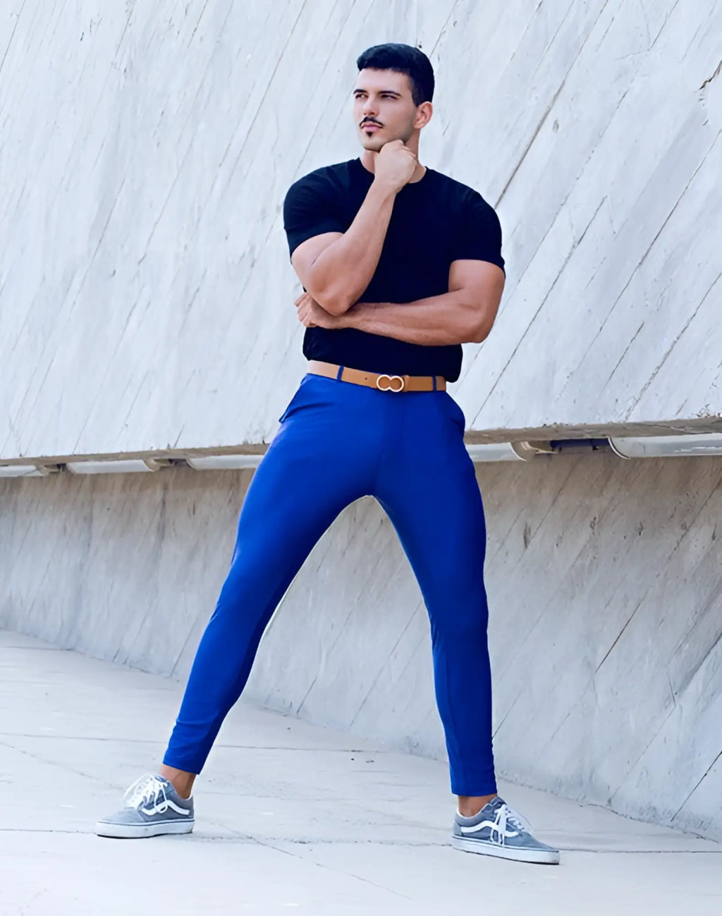 A man wearing 2EROS P60 Bondi navy form-fitting pants with a tan double buckle belt and gray Vans sneakers