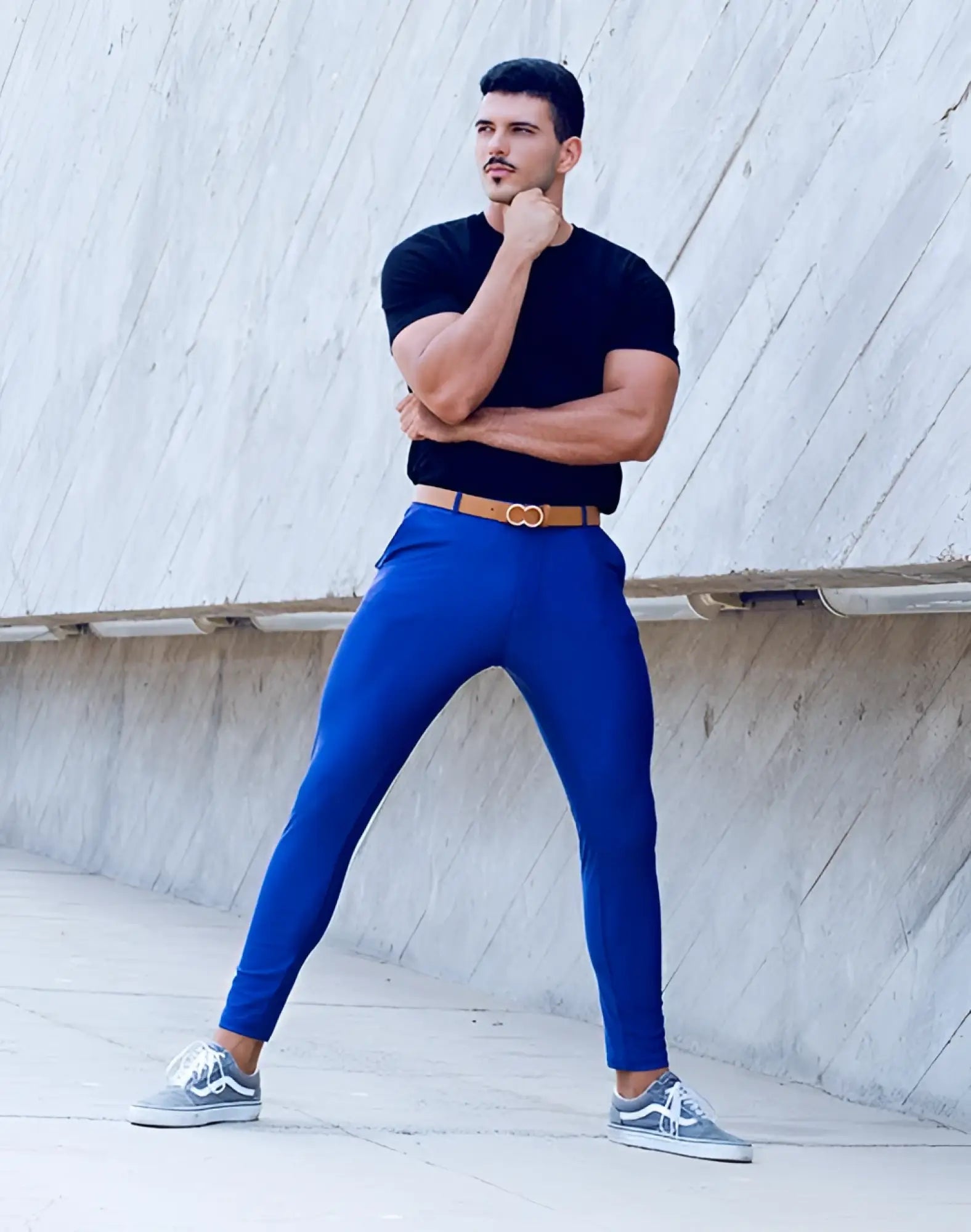 A man wearing 2EROS P60 Bondi navy form-fitting pants with a tan double buckle belt and gray Vans sneakers