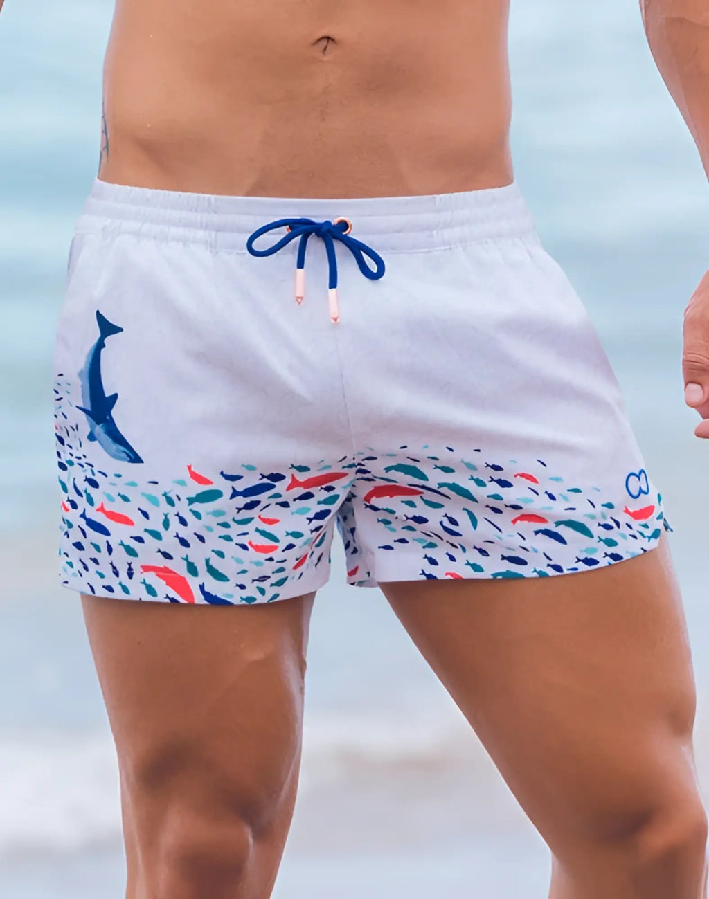White swim trunks by 2EROS with blue dolphin graphic and colorful fish pattern on hem featuring navy drawstrings