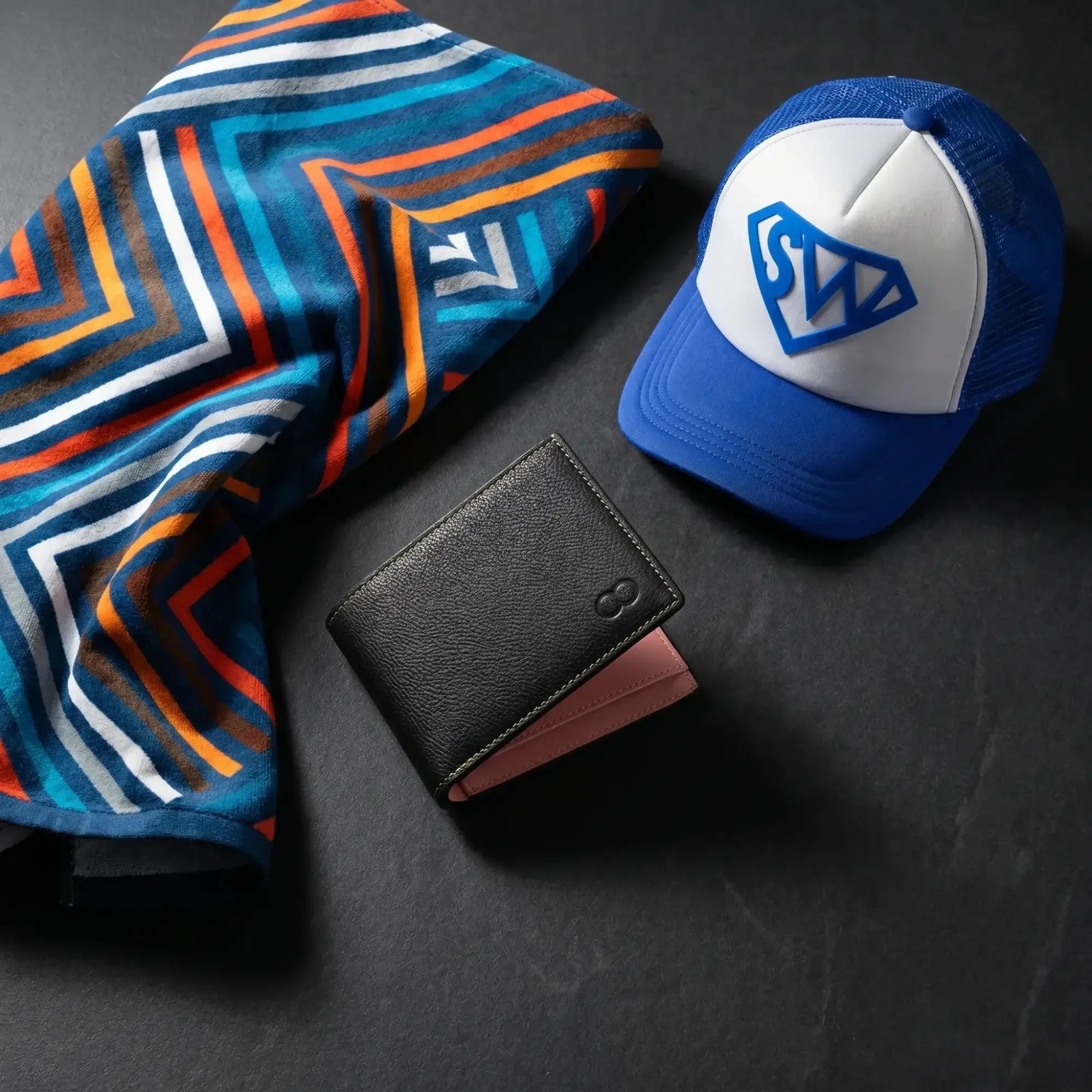 Black leather 2EROS RFID wallet with contrast pink interior, positioned near a patterned towel and blue trucker cap.