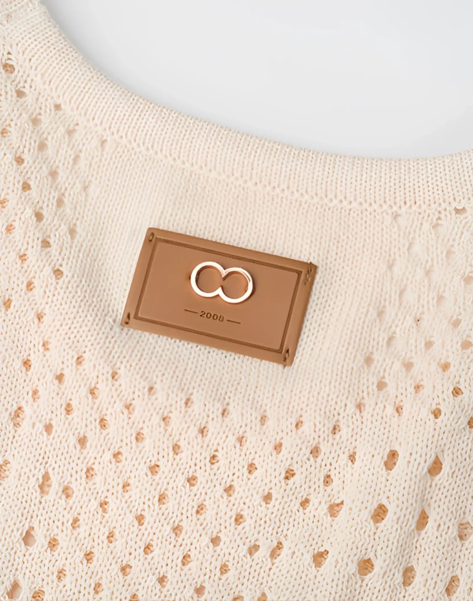 Beige knitted 2eros riviera singlet featuring a tan leather patch with an embroidered infinity symbol and year 2006