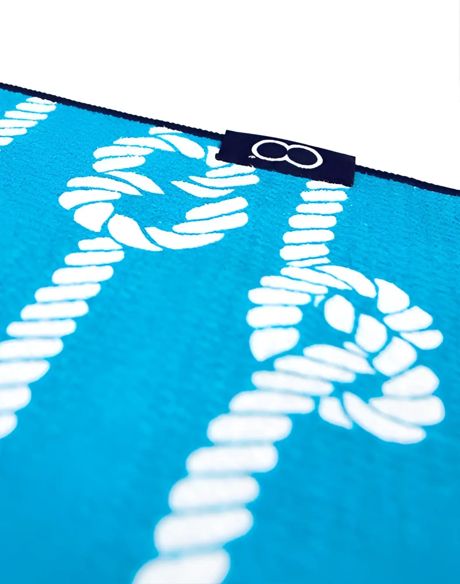 Bright turquoise 2EROS sand-free beach towel with bold white rope knot and chain pattern and navy blue brand tag 8