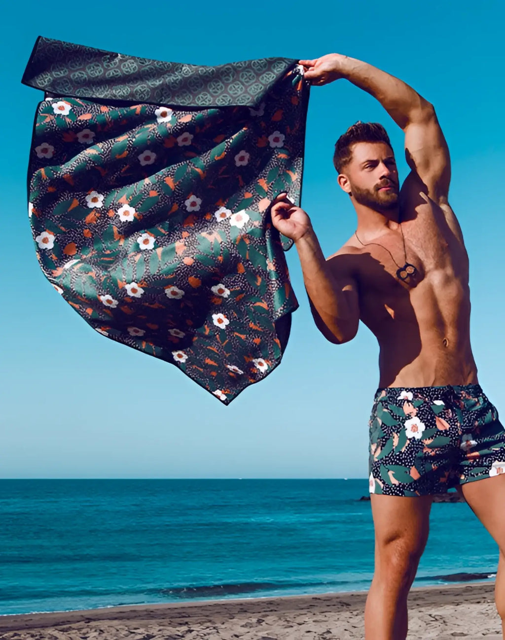 A dark green 2eros sand free beach towel with white and orange floral pattern and geometric border called night bloom