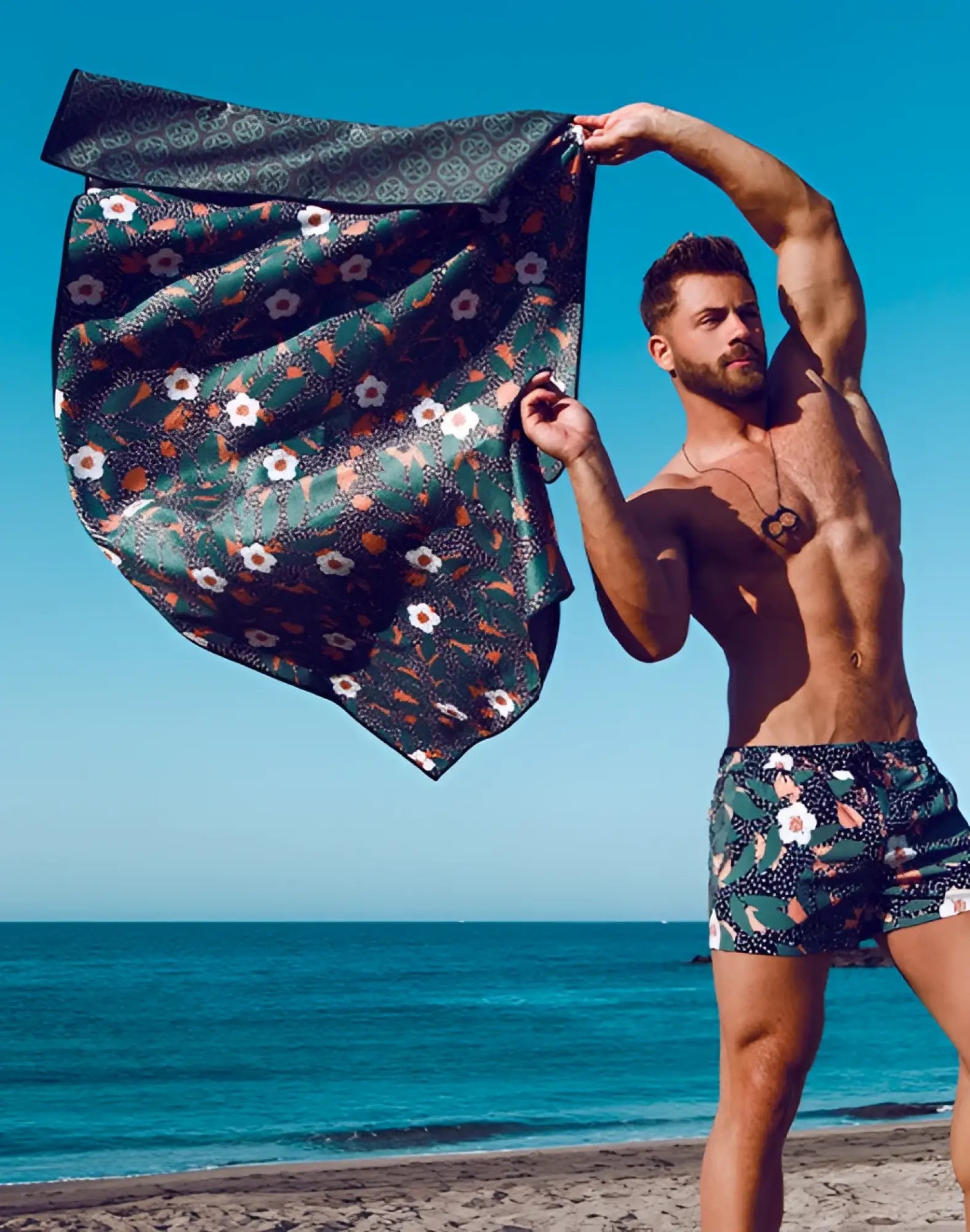 A dark green 2eros sand free beach towel with white and orange floral pattern and geometric border called night bloom
