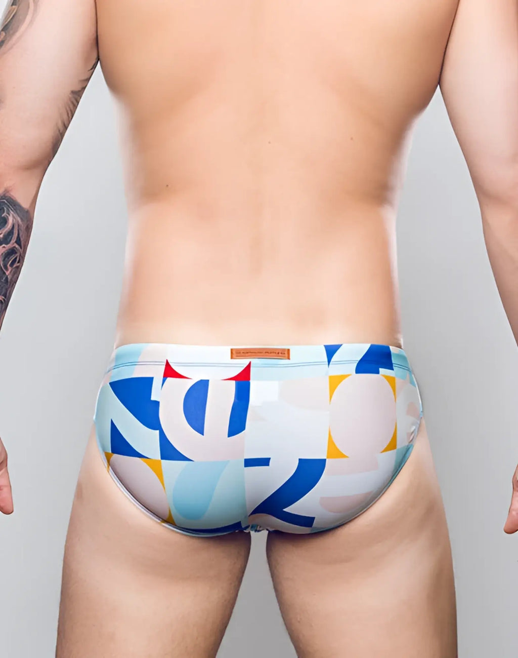 2eros v10 print swim brief in insignia turquoise with blue, white, and yellow geometric pattern and brown waistband label