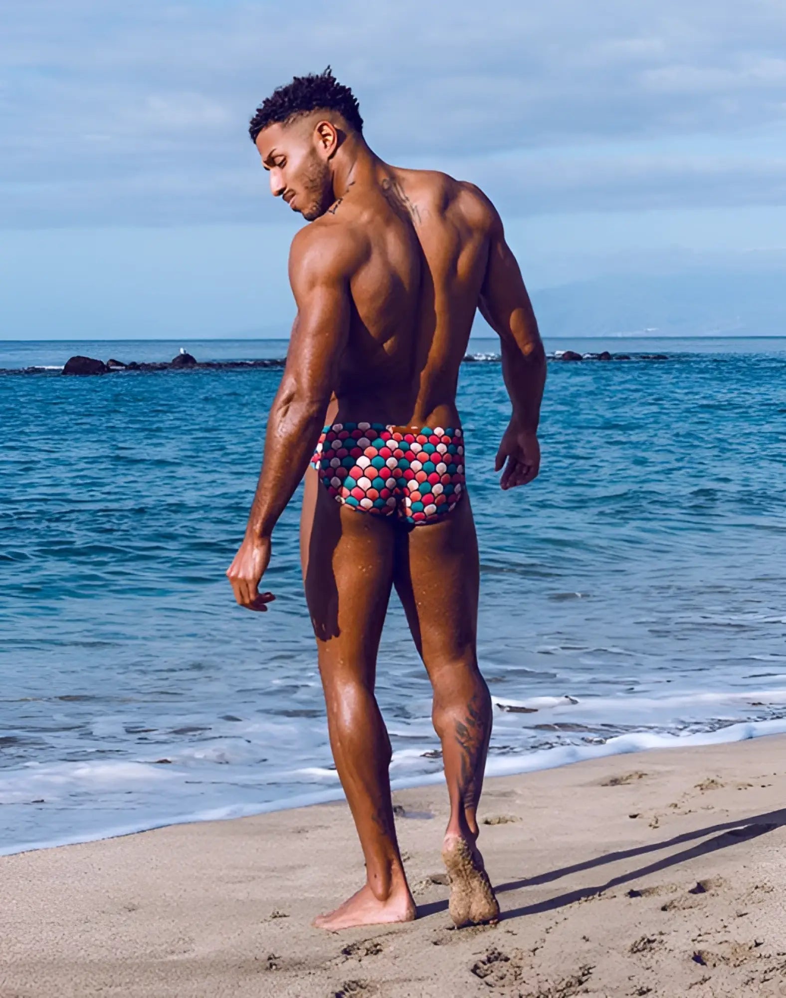 A man wearing 2EROS V10 print swim brief in retro red with a colorful geometric patterned design