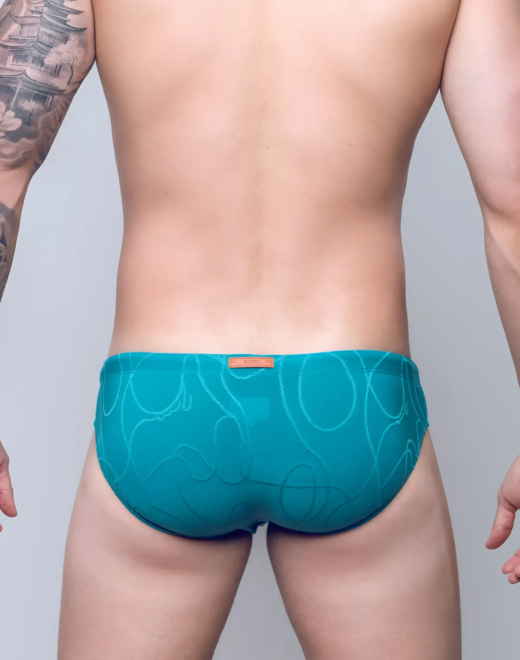 Teal textured 2EROS V10 swim brief with abstract pattern and orange brand tag at the waistband in ripple green
