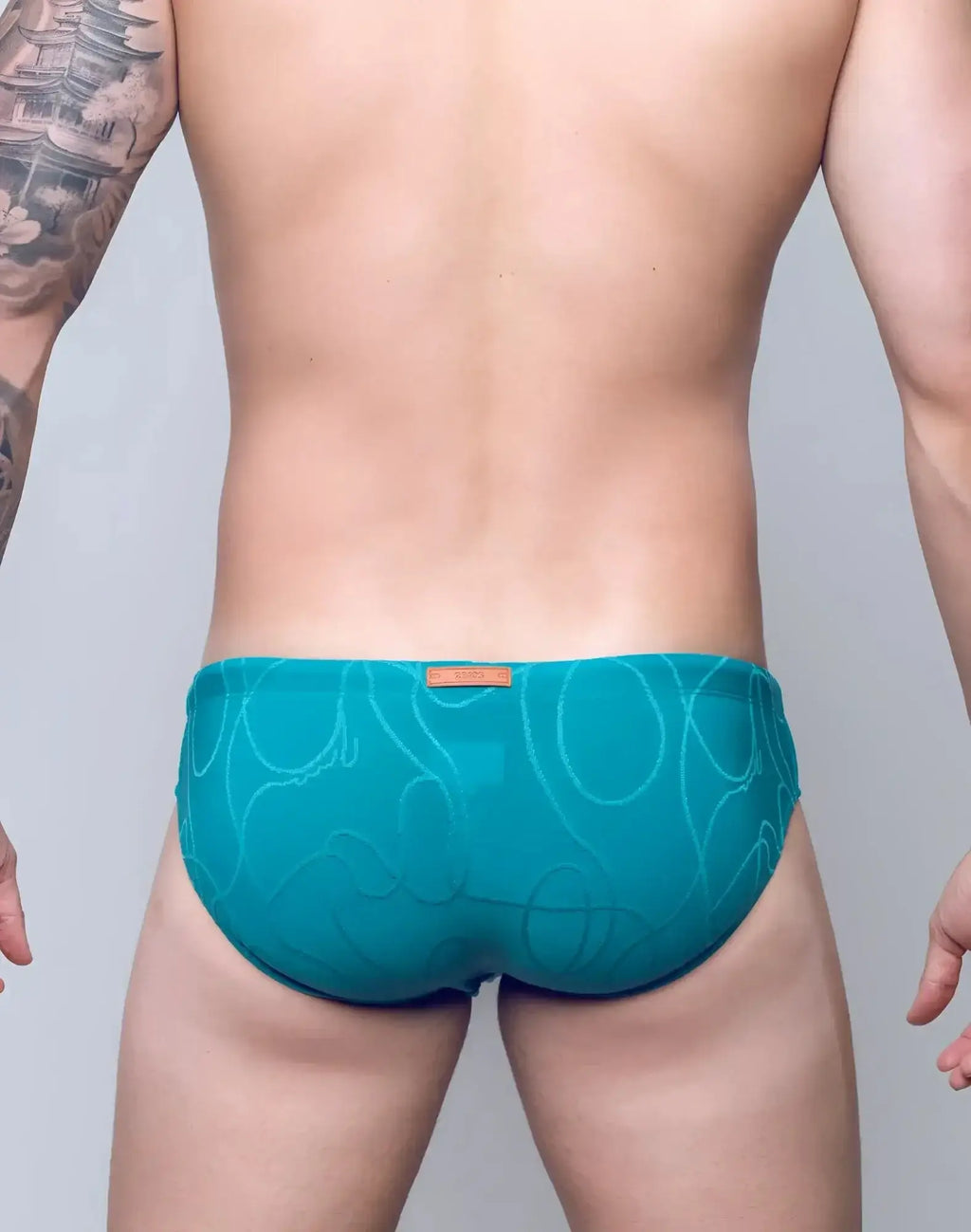 Teal textured 2EROS V10 swim brief with abstract pattern and orange brand tag at the waistband in ripple green