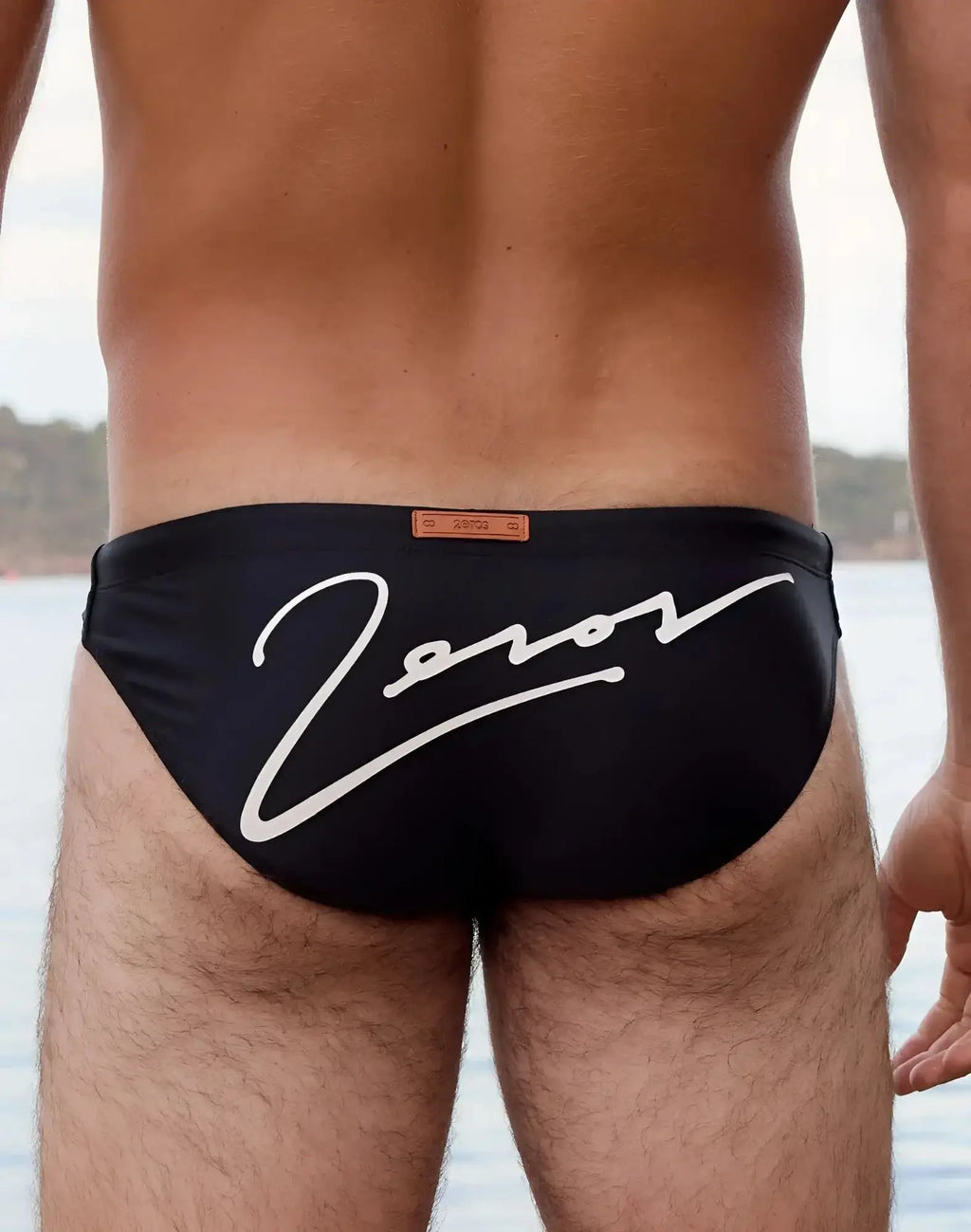 Back side of black 2eros v20 signature swim briefs with bold white cursive zorov logo and orange leather-like tag