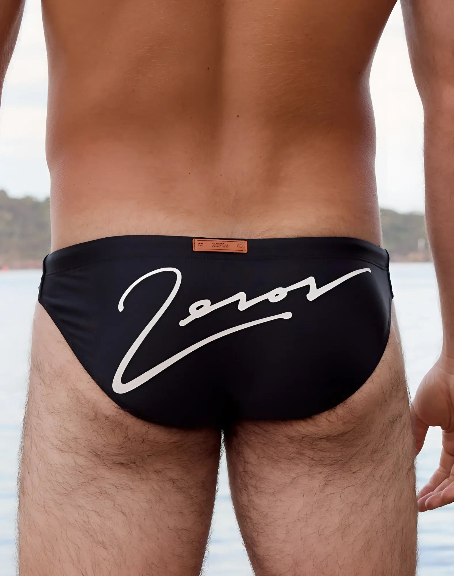 Back side of black 2eros v20 signature swim briefs with bold white cursive zorov logo and orange leather-like tag
