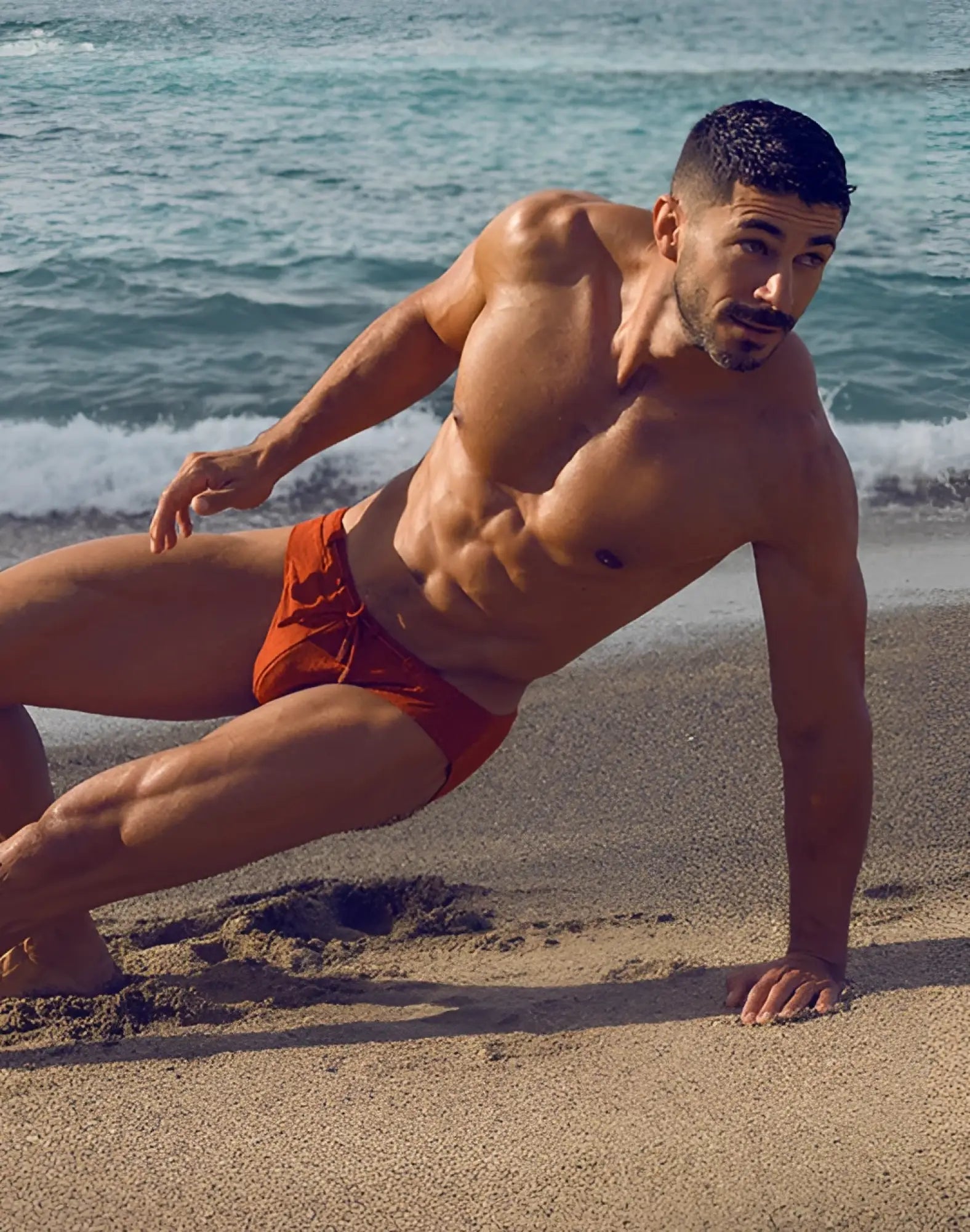 A man wearing 2EROS V30 textured swim brief in vibrant signet carmine orange with a tied waistband