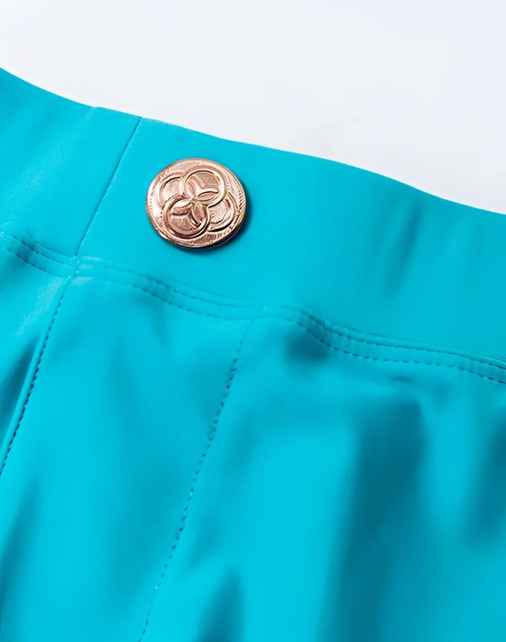 A metallic gold button with an intricate interlocking circle design on aqua 2EROS V60 Bondi swim trunks fabric