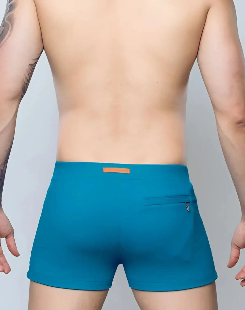 Back view of 2EROS V60 swim trunks in railroad teal with textured fabric, orange waistband label, and zippered back pocket