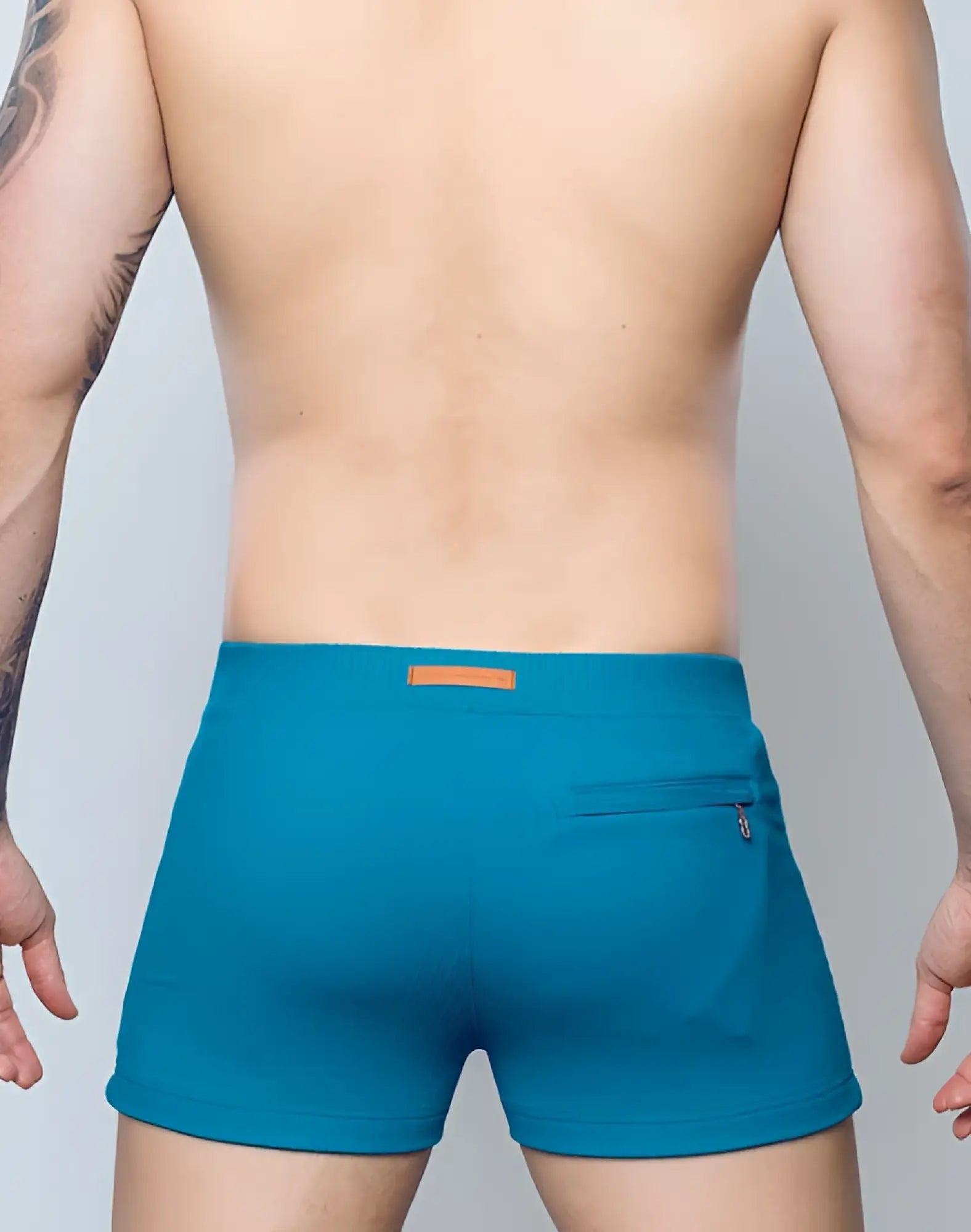 Back view of 2EROS V60 swim trunks in railroad teal with textured fabric, orange waistband label, and zippered back pocket