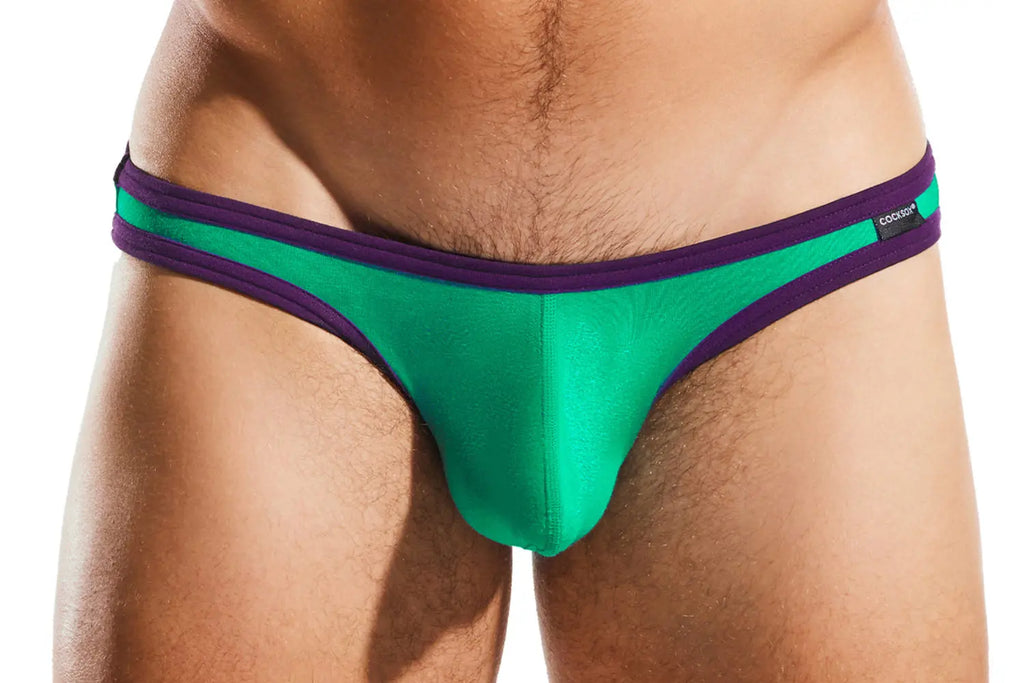 Close-up of a person wearing green briefs with purple trim on a white background.