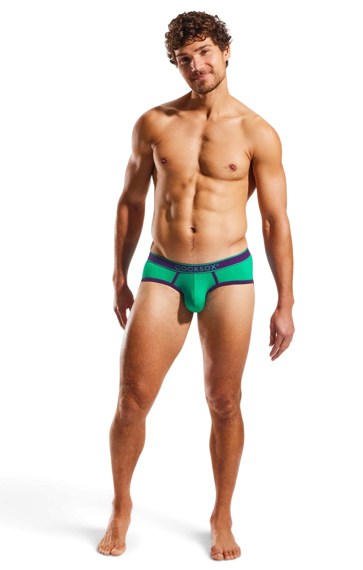 Shirtless man in green briefs with purple trim, standing on white.