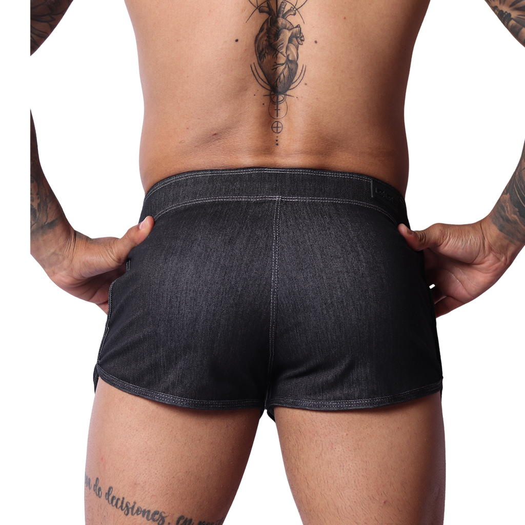 Back view of Gigo black denim hot shorts with visible contrast stitching, worn by a man against a black background.