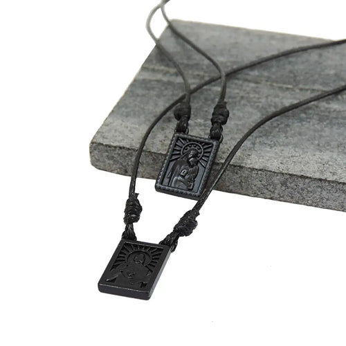 Two black cord necklaces with rectangular dark pendants on a grey block.